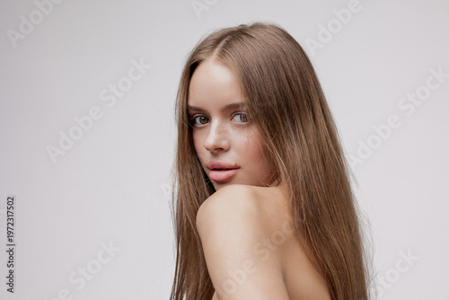 Young woman with long hair poses against a plain background in a studio setting