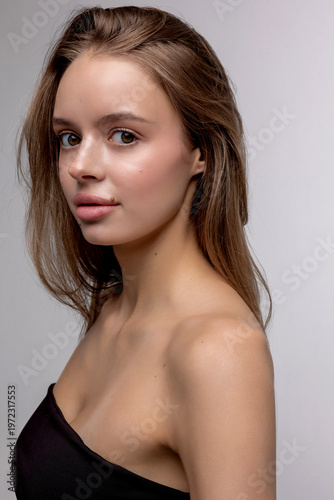 Young woman poses in studio with simple background and natural light showcasing her features and hair