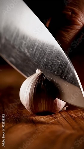 Fresh garlic bulb ready for slicing on wooden board with sharp kitchen knife