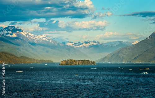 Majestic Alaskan fjord landscape with floating ice, forested island and towering mountains
