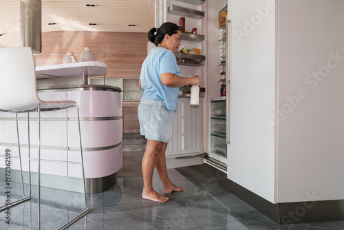 Woman in kitchen takes milk from refrigerator during afternoon