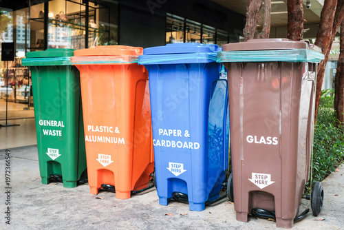 Recycling bins for different materials placed outside a shopping center in the afternoon