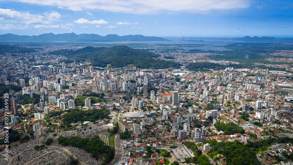 Fototapeta premium Aerial view of Joinville with dense urban area, green hills and Babitonga Bay in the background, Santa Catarina.