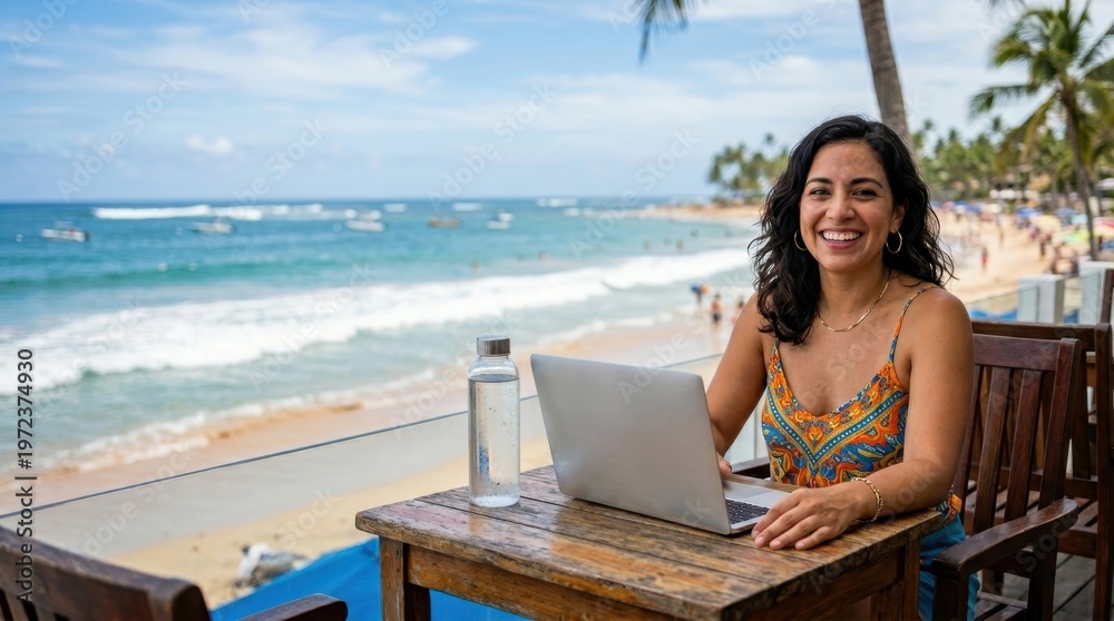 Fototapeta premium the 31-year-old latina woman is framed boldly at her small table, with her laptop and water bottle prominently placed, set against a backdrop of waves and sandy beach