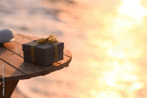 Bild auf Leinwand Close-up of small gift box on wooden table, with soft golden glow of sunset over water