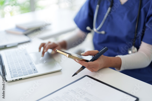 Medical professional adult female hands using laptop computer smartphone pen working researching patient data at hospital clinic office desk for healthcare documentation