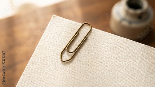 Heavily textured blank linen paper document secured by an antique brass paperclip visualizes the attachment of traditional legal agreements.