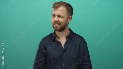 Foto Man with beard and visible chest smiling with slight head tilt wearing a navy shirt in teal studio; friendly