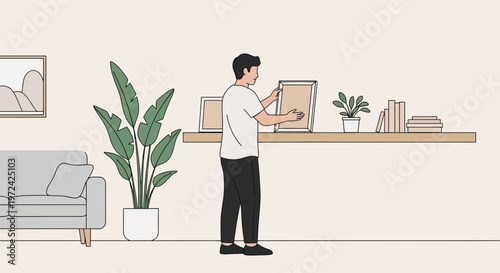 Man arranging framed pictures on a shelf in a modern living room with plants