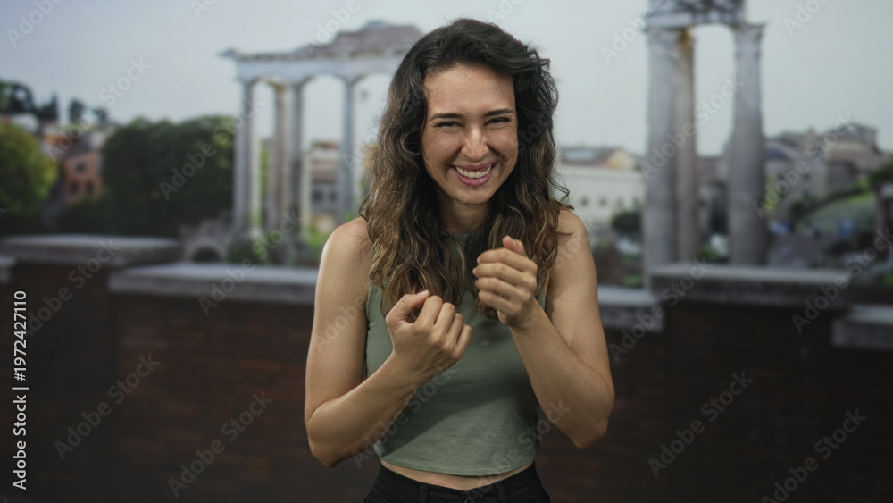 Fototapeta premium Young hispanic smiling woman points finger to historic building on street framed by ancient columns; joy.