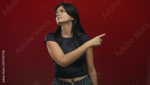 Tablou pe pânză Young hispanic woman flicks finger dismissively in red studio with skeptical expression; defiance rejection