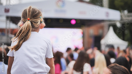 Little girl watching outdoor summer concert from audience at music festival