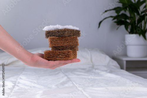 Photography Woman's hand holding layers of coconut coir, cotton and horsehair above a bed with a white blanket