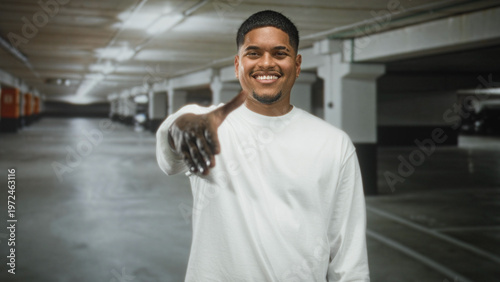 Foto Man extends hand for handshake in building parking garage, smiling with beard and white shirt; welcome greeting