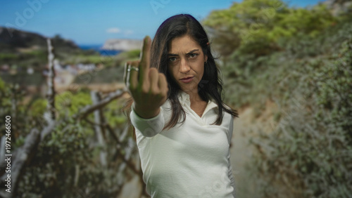 Tableau sur toile Woman shows middle finger toward camera on forest path wearing white shirt and rings while staring directly; defiance protest