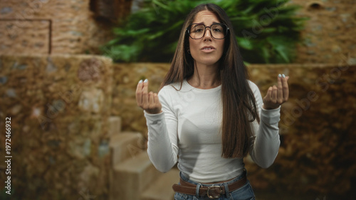 Tableau sur toile Woman wearing glasses and white top with cupped hands making a beckoning gesture in stone building courtyard with visible stairs; invitation longing
