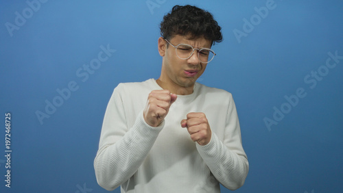 Tableau sur toile Man with clenched fists and eyeglasses standing in a studio setting against a vibrant blue backdrop; disgust