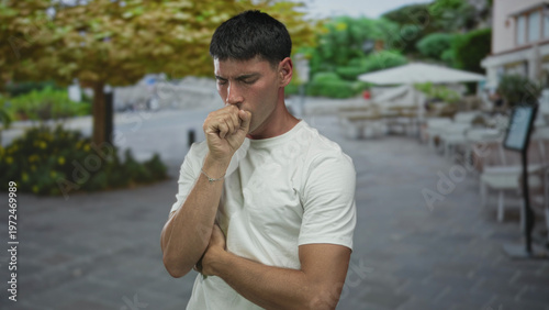 Obraz na płótnie Man with hand to mouth coughing at outdoor restaurant terrace street scene; health concern and vulnerability