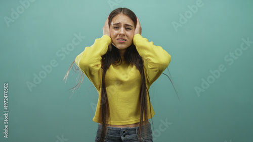 Foto Girl pressing hands to ears with pained expression and visible midriff in studio wearing yellow sweater and denim jeans, long hair; distress