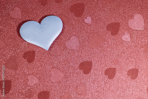A white paper heart lies on a red background with other red hearts. Valentine's Day