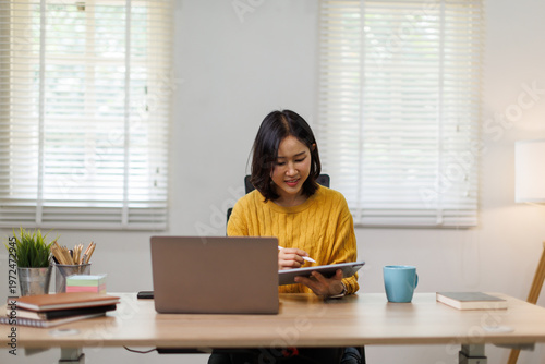 Foto Young Asian woman sitting at a desk, digitally drawing or writing