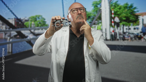 Man doctor holds a trial frame near his eye, touches chin in a measured gesture during on street vision measurement test; curiosity clinical testing.
