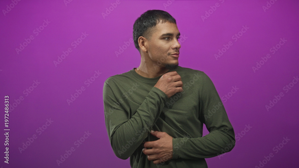 Obraz premium Man in green shirt holding his wrist and folding arms against a purple studio backdrop; quiet introspection calm.