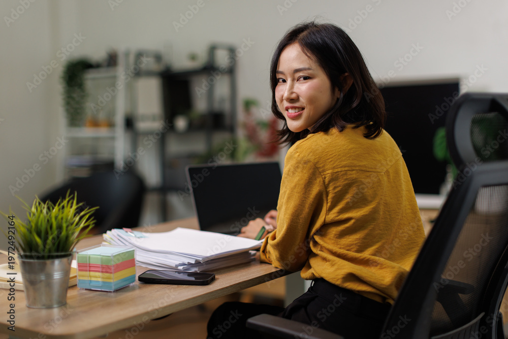 Obraz premium Young Asian woman smiling while working on a laptop