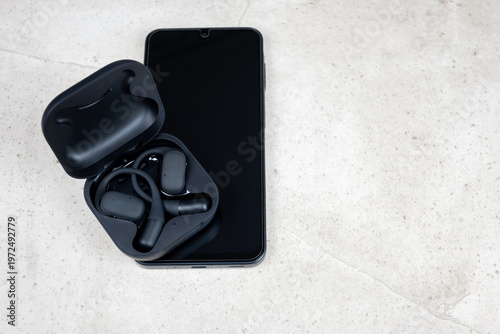 Black wireless headphones and mobile phone. New earphones and black smartphoneon the stone table. New technologies.
