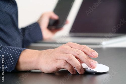 Businessman Using Computer Mouse While Holding Smartphone at Desk