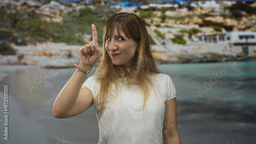 Photos Woman pointing index finger toward camera in studio setting with seaside backdrop and white t shirt visible; playful confidence