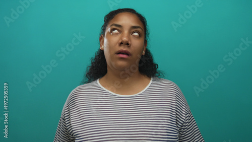 Billede på lærred African american woman wearing striped shirt rolls eyes with slight frown in studio with teal background; annoyance