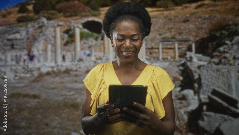 Fototapeta premium Woman holds tablet with both hands, tapping screen while standing among ancient ruins building and reading; curiosity travel discovery.