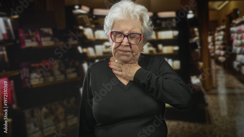 Photos Senior woman holding hand to throat and grimacing among pharmacy shelves and product aisles in a store interior; anxiety concern