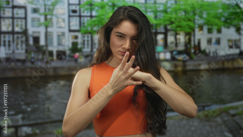 Принти на полотні Young hispanic woman slams fist against palm on street by river canal lined with buildings; anger frustration
