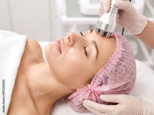 Woman receiving a non-invasive facial rejuvenation treatment with a professional device at a beauty clinic