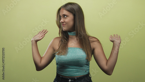 Fotografia Woman shrugging palms up with a coy smirk, turquoise strapless top and choker visible in a midshot against a green studio wall, hands raised in a questioning gesture; uncertainty