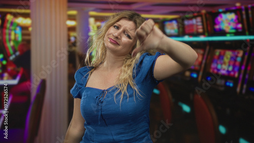 Woman giving thumbs down gesture inside casino building near slot machines and gaming chairs; disappointment bad luck.