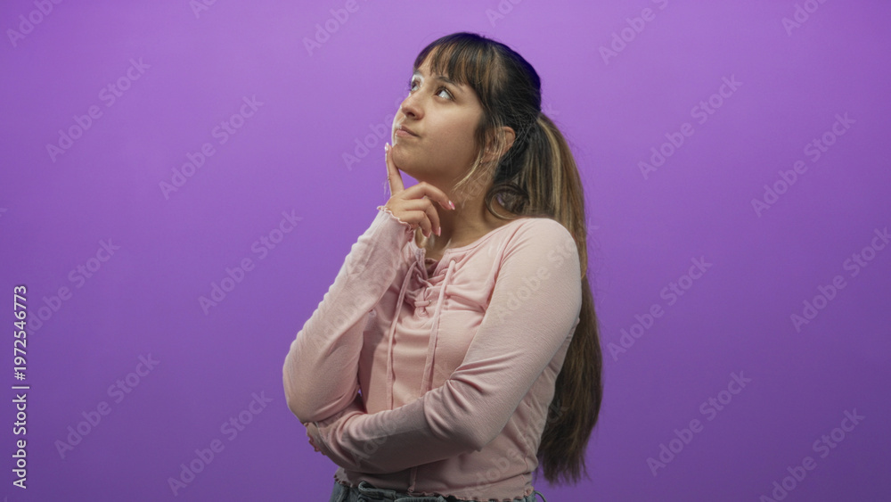 Fototapeta premium Woman with hand on chin and squinting gaze, crossed arms and casual pink shirt in studio; pensive reflection.