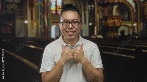 Tableau sur toile Man smiling and giving thumbs up gesture while placing hand on chest inside ornate church building with pews and stained glass; gratitude faith devotion