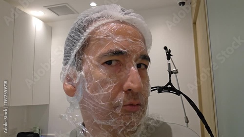 Treatment, cure of face skin in dermatology clinic. Acne Scars laser procedure for man. Man with cream with anesthesia and plastic film on his face before laser therapy procedure.