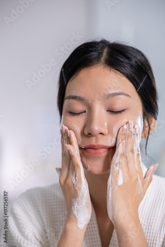 Foto Beautiful young Asian woman washing face with cleansing foam enjoying morning se