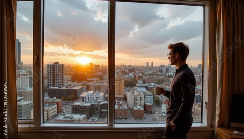 Man Viewing Sunset Over Cityscape from Hotel Room Window While Holding a Coffee Mug