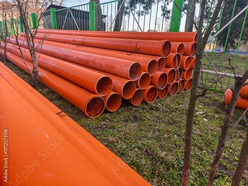Long row of orange plastic pipes arranged outdoors showing construction materials and infrastructure equipment in industrial environment perspective view