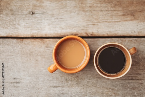 Top view of two coffee cups—one black and one with cream—side by side on a rustic light wood table.