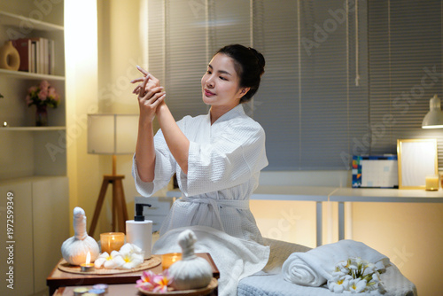 Woman in bathrobe applying essential oil during her skincare routine at beauty spa salon. Spa beauty treatment concept. Body skin care