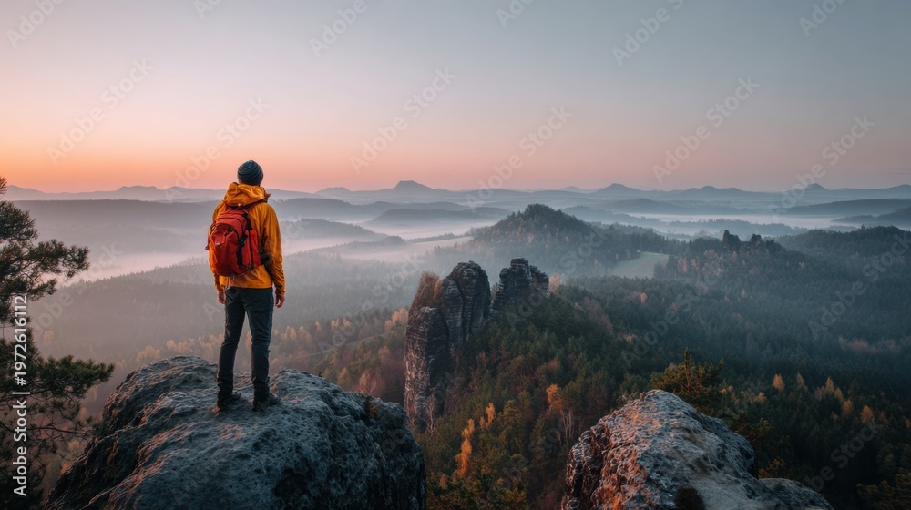 Fototapeta premium A traveler stands at a viewpoint with a backpack, gazing at the expansive landscape during golden hour light, surrounded by mountains and forests.