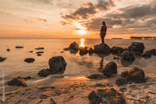 A woman stands on a beach with a sunset in the background