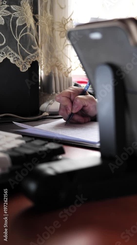 A close-up of the hand of a woman with nail dystrophy writing with a pen in a notebook while sitting at a table.