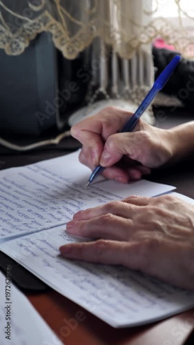 A close-up of the hand of a woman with nail dystrophy writing with a pen in a notebook while sitting at a table.
